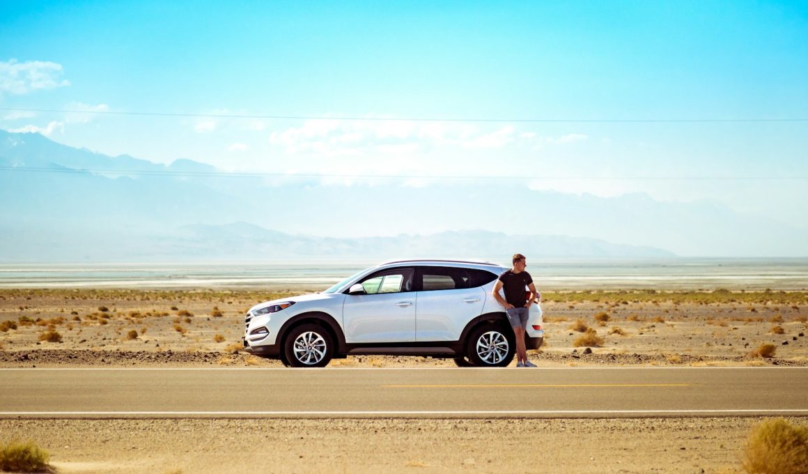 man standing beside white SUV near concrete road under blue sky at daytime