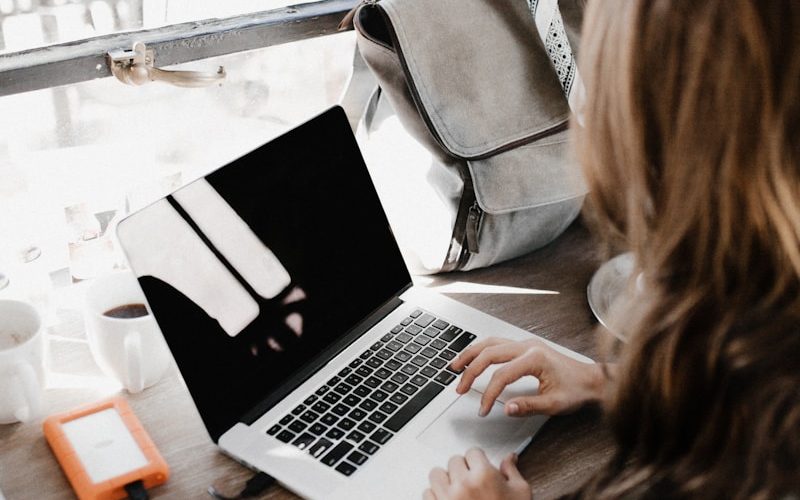 girl wearing grey long-sleeved shirt using MacBook Pro on brown wooden table