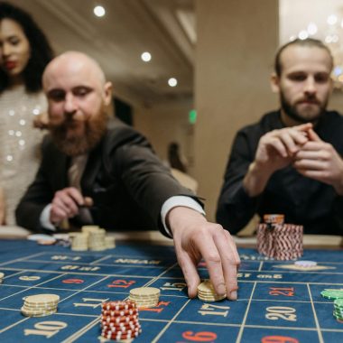 Three adults playing roulette at a casino, focused on placing bets with gaming chips.