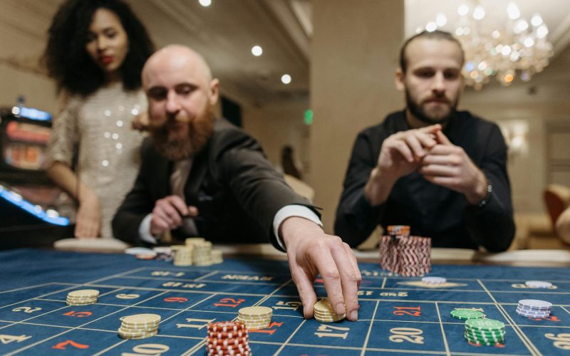 Three adults playing roulette at a casino, focused on placing bets with gaming chips.