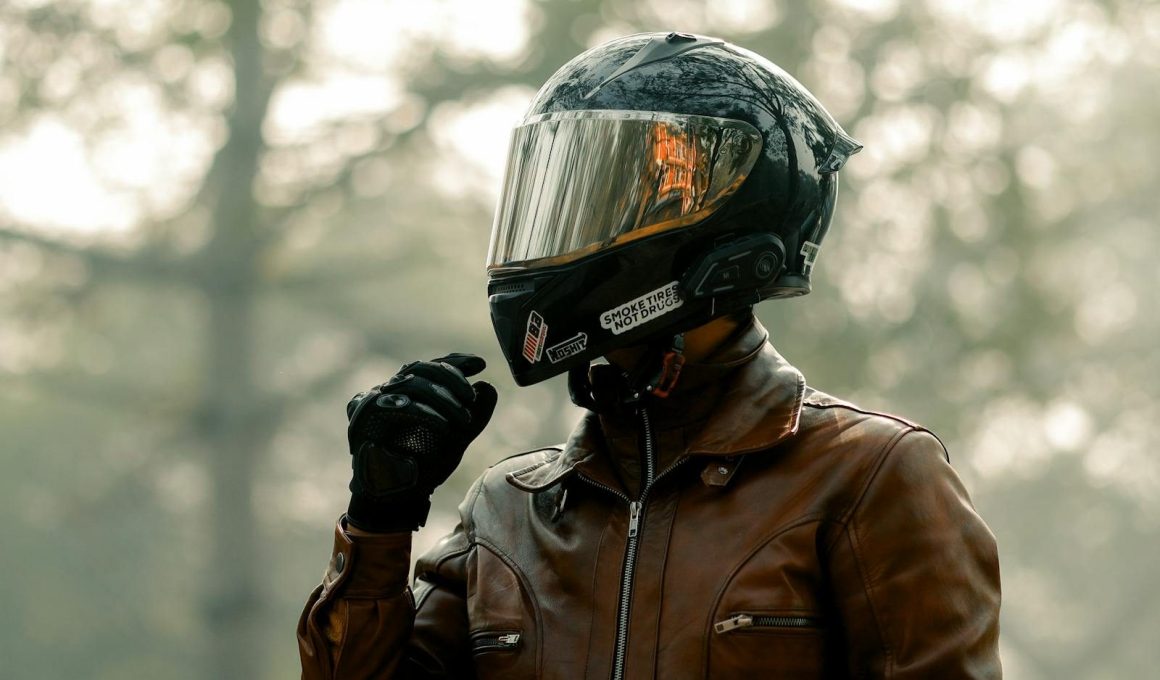 Biker wearing helmet and leather jacket in a foggy forest, evoking adventure.