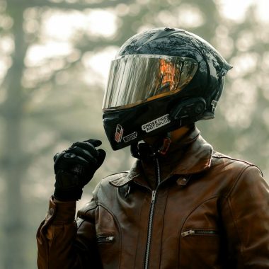 Biker wearing helmet and leather jacket in a foggy forest, evoking adventure.