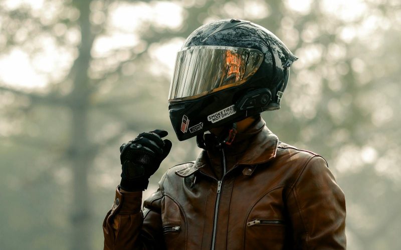 Biker wearing helmet and leather jacket in a foggy forest, evoking adventure.