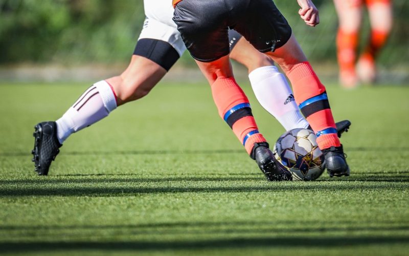 woman in black and white soccer jersey kicking soccer ball on green field during daytime
