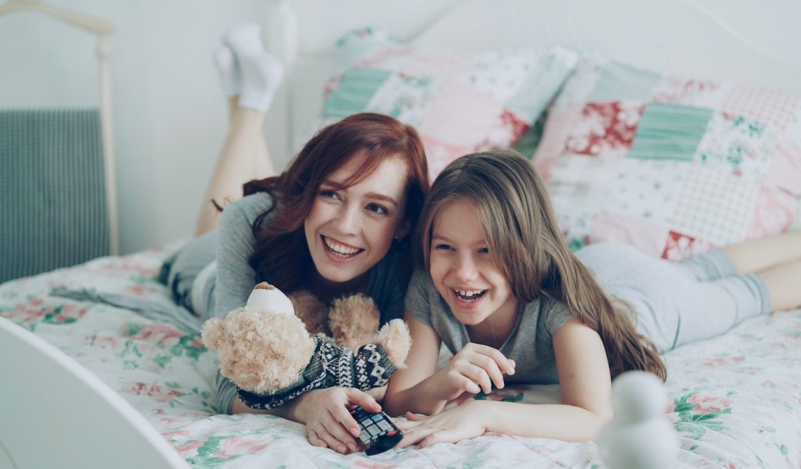 Two girls laugh while relaxing on a bed.