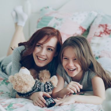 Two girls laugh while relaxing on a bed.