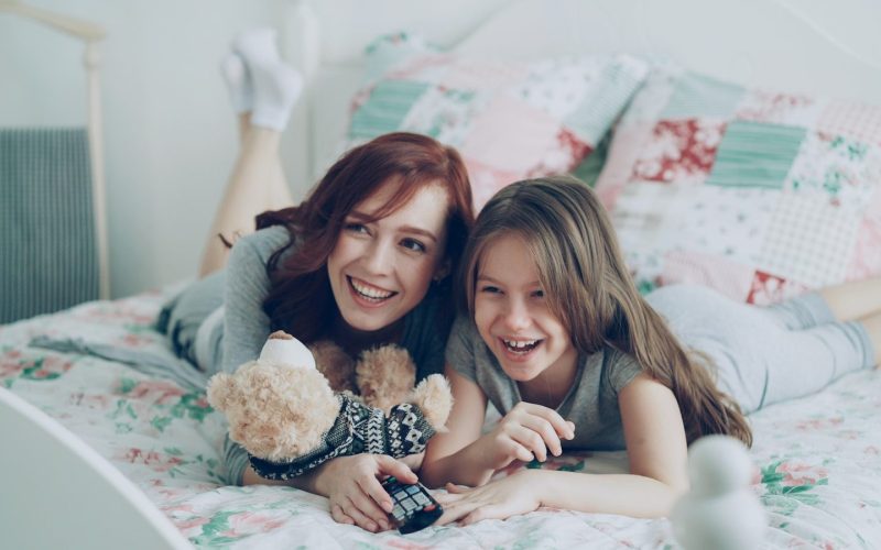 Two girls laugh while relaxing on a bed.