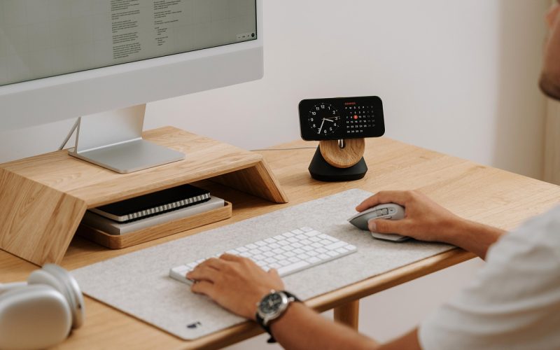 Man aan een opgeruimde thuiswerkplek met laptop op standaard en bureaulamp