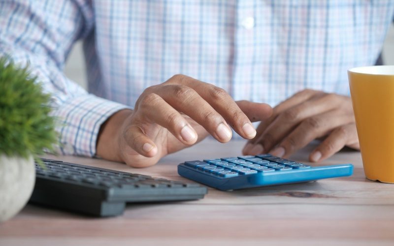person using calculator at desk with coffee mug