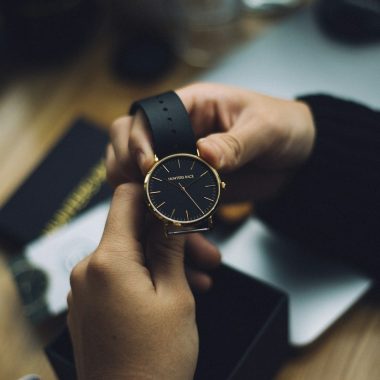 person holding gold-colored analog watch with black strap